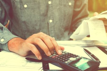 FAQ: Wie finanziere ich mein Studium? Student hält in einer Hand Abrechnungen, mit der anderen tippt er auf einem Taschenrechner