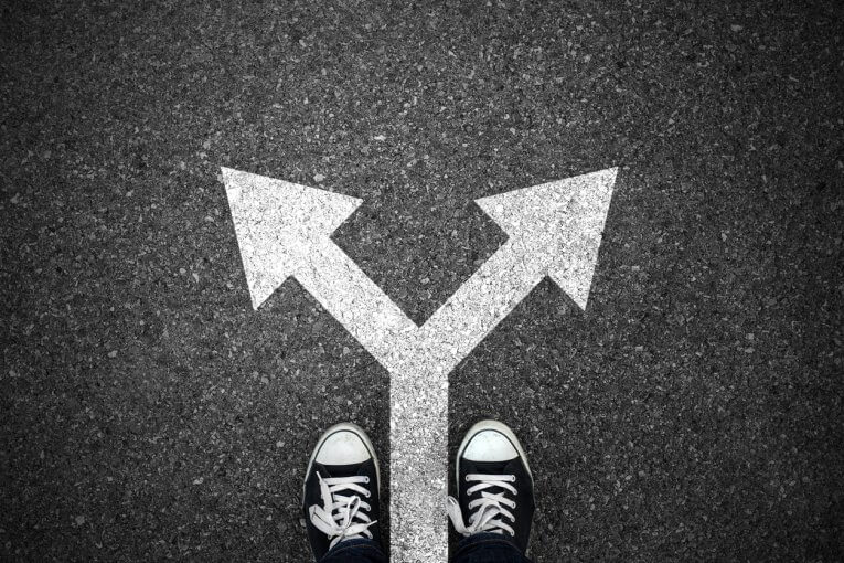 Schülerfrage: Eher Ausbildung oder Studium? Zwei Füße stehen an zwei Pfeilen, die auf den Boden gemalt sind und in unterschiedliche Richtungen zeigen