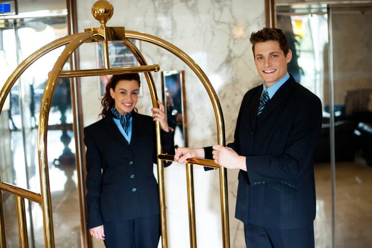 Zwei Hotelmitarbeiter stehen mit einem Gepäckwagen im Eingangsbereich eines Hotels
