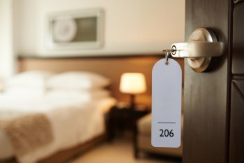 Offene Hotelzimmertür, in der noch der Schlüssel steckt, mit Blick aufs Bett 