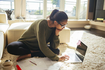 Frau sitzt mit einem Laptop auf dem Boden in ihrer Wohnung und informiert sich im Internet