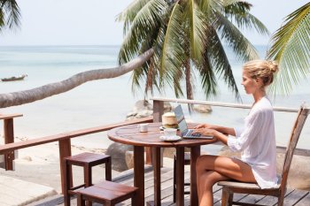 Studentin sitzt am Strand auf Terrasse und arbeitet am Laptop