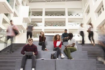 Studenten sitzen in Hochschul-Foyer auf Treppenstufen
