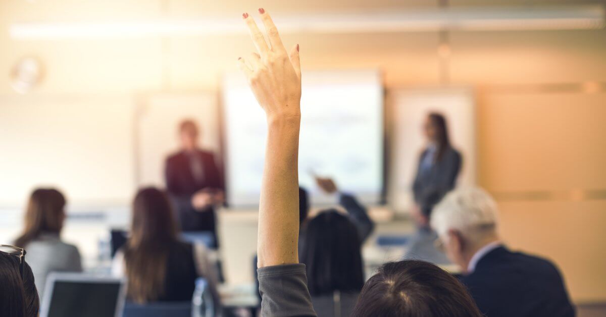 Seminarsituation mit Blick auf Dozent und Tafel, eine Teilnehmerin meldet sich